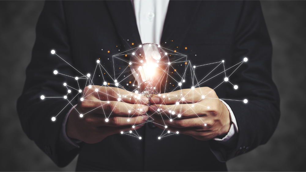Business man in suit holding a light globe with virtual networking paths indicating ideation and creativity